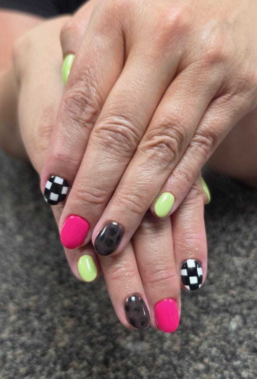 Colorful nails with checkerboard, polka dot, lime green, and pink designs on hands.