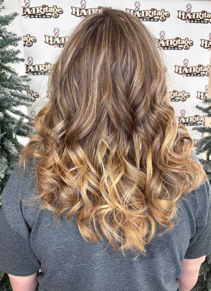 Curly, layered hairstyle with blonde highlights, photographed from the back in a salon.