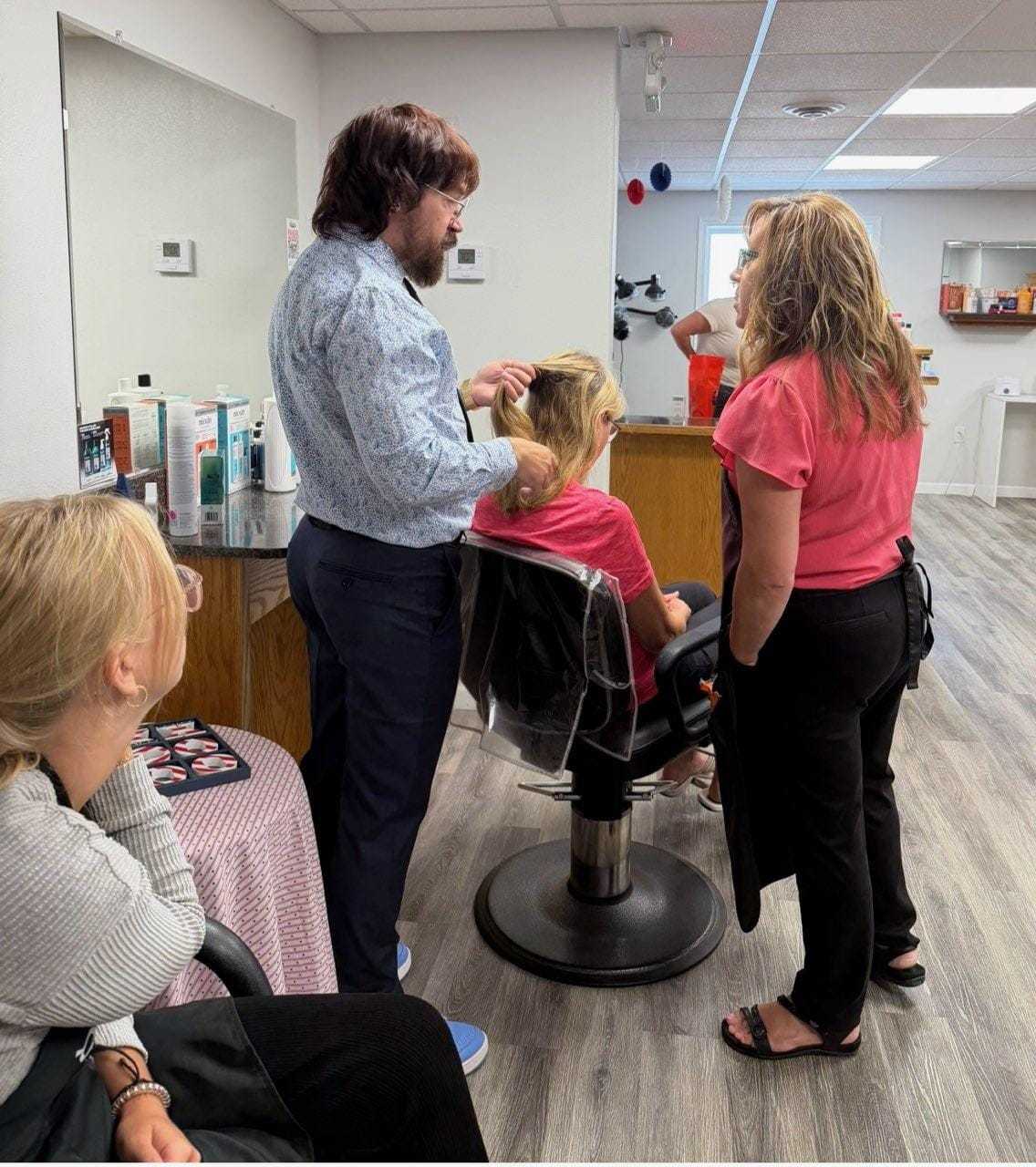 Busy hair salon scene with hairstylist working on a client's hair, surrounded by onlookers.